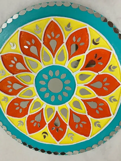 A close-up of a vibrant mirror art piece with a floral motif in yellow, orange, and teal.