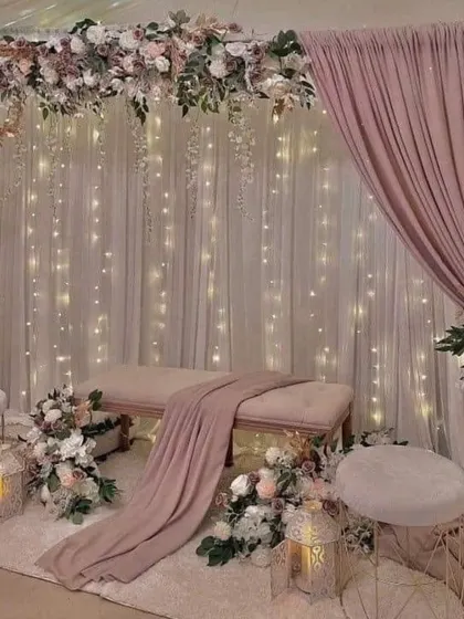 A dreamy and romantic setup in pastel pink tones. This decoration features a floral arch, fairy light curtains, and elegant seating, perfect for an engagement or intimate reception.