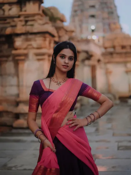 A moody and atmospheric shot of a model in a traditional saree against the backdrop of a historic temple at dusk. The lighting creates a sense of drama and timelessness.