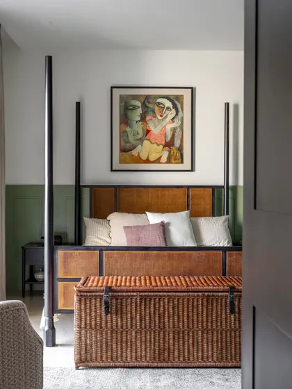A full view of the primary bedroom, showcasing the four-poster bed with a cane headboard and a colorful piece of art. The design combines bold color with natural textures for a soft yet interesting presence.