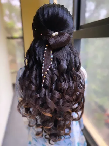 A half-up style featuring a hair bow and a cascade of curls, with a delicate strand of pearls woven through. This is a detailed and romantic look taught in my advanced classes.