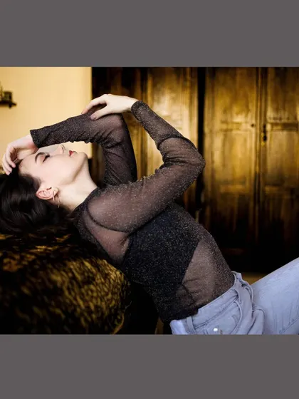 A cozy and intimate portrait of a model in a sheer top, relaxing in a warmly lit home environment.