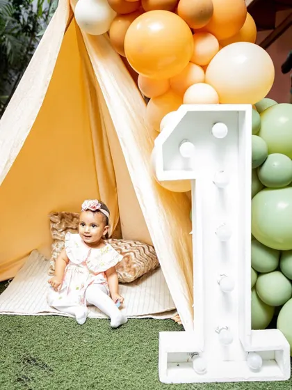 This little girl is enjoying her boho-themed first birthday party, complete with a teepee and a giant light-up number one.
