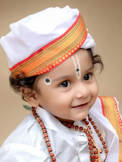 A sweet and gentle portrait of a baby dressed as a Varkari devotee. The soft lighting highlights the child's features and the simplicity of the attire.