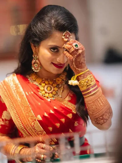 A playful moment captured beautifully. The intricate gold work on her custom red blouse shines as she gets ready for the celebration.