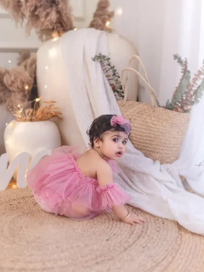 A baby girl in a pink tulle romper explores the bohemian-themed setup during her first birthday shoot. The natural textures and soft lighting create a warm and inviting scene.