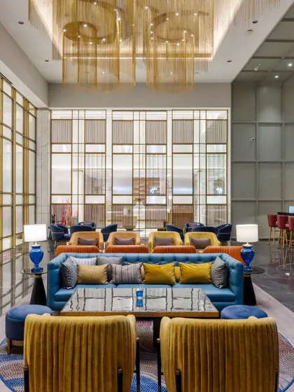 The vibrant lounge at Holiday Inn, Lucknow, showcasing a dynamic interplay of color and texture. We designed this public space with varied seating arrangements, from plush blue sofas to mustard yellow armchairs, to foster social interaction while intricate metal screens provide a sense of privacy.