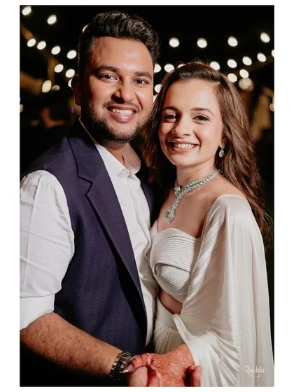 A close-up of the happy couple at their dinner event. Her modern white outfit and diamond jewelry pair beautifully with his tailored waistcoat, showing how contemporary looks can still feel special and celebratory.