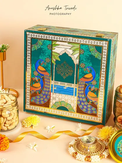 A closed view of an ornate peacock-themed Diwali hamper box, surrounded by festive elements to highlight its beautiful design.