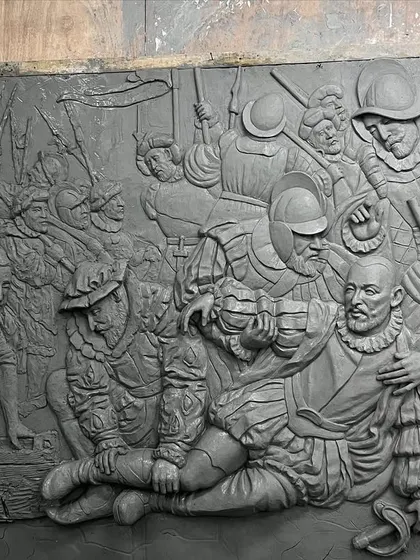 An angled view of the clay sculpture, showing the complex layering of figures to create a sense of a chaotic battle scene.