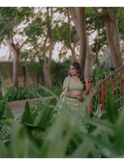 A quiet, pensive portrait of the bride amidst lush greenery, her green lehenga blending beautifully with the natural surroundings.