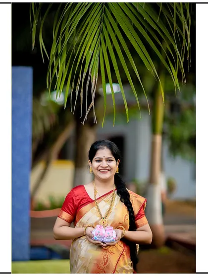 A happy mom-to-be in a traditional saree, proudly holding up a pair of pink baby booties.