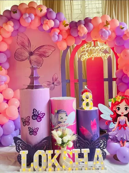 A beautiful fairy and butterfly themed eighth birthday party. The setup features a pink and purple balloon arch, character cutouts, and marquee letters.