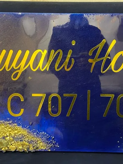 A close-up of the navy blue and gold 'Luyani House' nameplate, showing the reflection on the glossy resin surface.