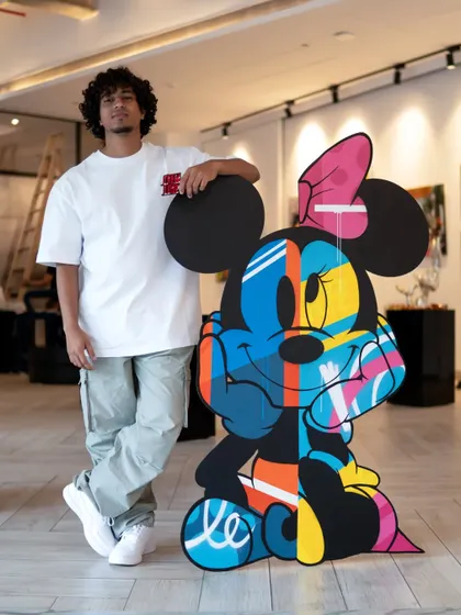 Standing with my finished Minnie Mouse artwork. This piece is huge, standing 55 inches tall, and uses vibrant spray-painted colors on layered MDF to bring her to life.