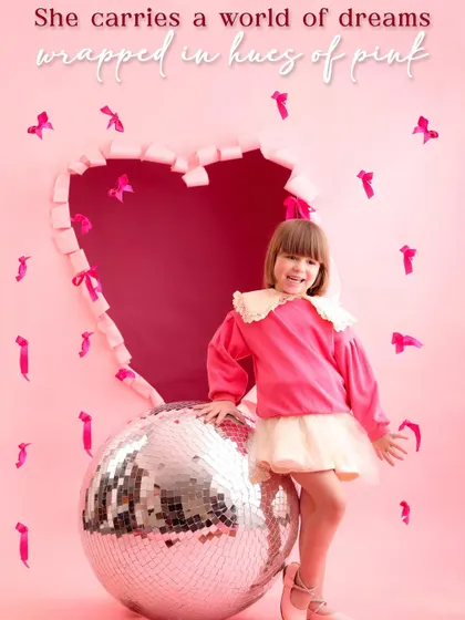 A world of pink and sparkle for Valentine's Day. This young girl poses with a giant disco ball in front of a heart-shaped cutout, creating a fun and modern festive portrait.