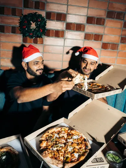 Merry Crustmas! The founders share a slice during the holidays, surrounded by pizza boxes ready for a festive feast.