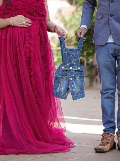 It's a boy. This creative shot focuses on a pair of tiny denim overalls held by the parents-to-be, a charming way to reveal the baby's gender.