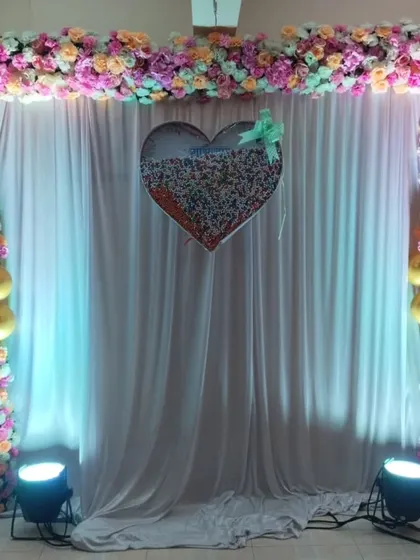 A simple yet elegant naming ceremony backdrop made with a floral frame, a white curtain, and a sequin heart centerpiece.