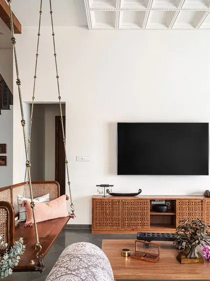 The living room is a perfect blend of comfort and tradition, featuring a classic wooden swing and a media cabinet with intricate jaali work.