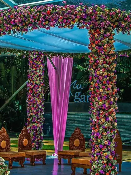 An incredibly lush and colorful wedding mandap. The pillars and canopy are completely covered in a dense arrangement of multi-colored flowers, creating a spectacular floral haven for the ceremony.