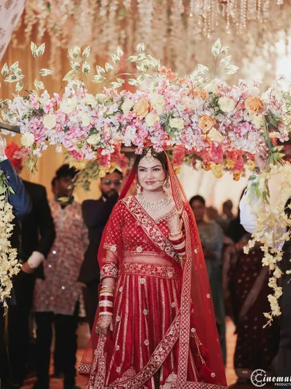 A beautiful shot of the bride walking under the phoolon ki chadar, looking directly at the camera with a confident smile.