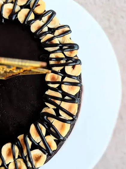 A close-up aerial view of the Ferrero Rocher cake, showing the border of toasted hazelnuts and the rich, glossy chocolate ganache top.