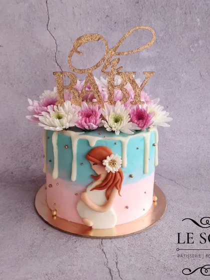 My most popular baby shower design. This 1 kg Chocolate Truffle cake features a pink and blue theme, a white chocolate drip, and a beautiful 2D figurine of a pregnant mother, all topped with fresh flowers.