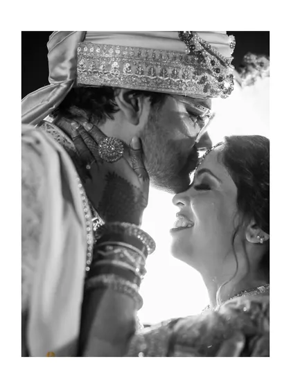 A powerful black and white shot of a groom kissing his bride's forehead. This timeless photo from their wedding day captures a moment of pure love and happiness.