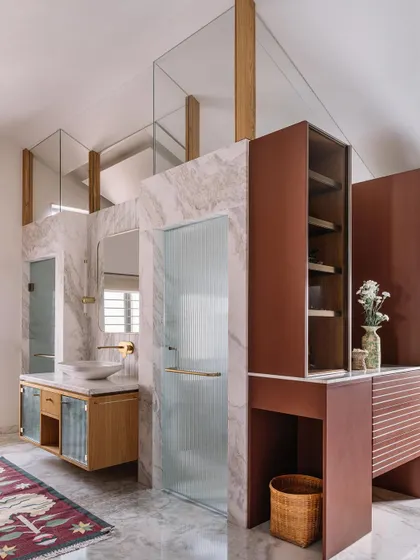 In this spacious bathroom in Cocoon House, we used marble and textured glass to create distinct zones for the vanity and shower areas. The design plays with height and light, featuring a custom reddish-brown vanity that adds a bold stroke of color to the otherwise neutral space.