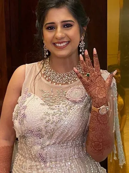 A happy client showing off her beautiful floral mehendi at her engagement party. The design extends up her forearm, complementing her elegant gown.