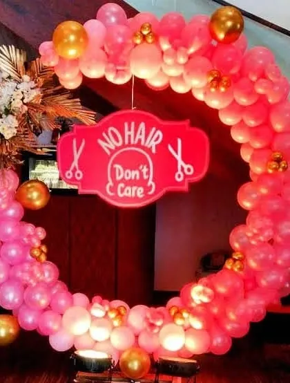 A slightly different angle of the pink and gold 'No Hair Don't Care' mundan party setup. The lighting from below makes the pink balloons glow, creating a warm and festive look.
