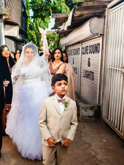 The bride and her entourage make their way to the church through a narrow lane, a classic Mumbai wedding scene.