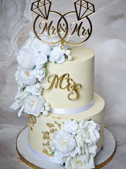 Another view of this stunning ivory and white two-tier cake, featuring a custom "Mr & Mrs" ring topper. This design is perfect for an intimate wedding or engagement party.
