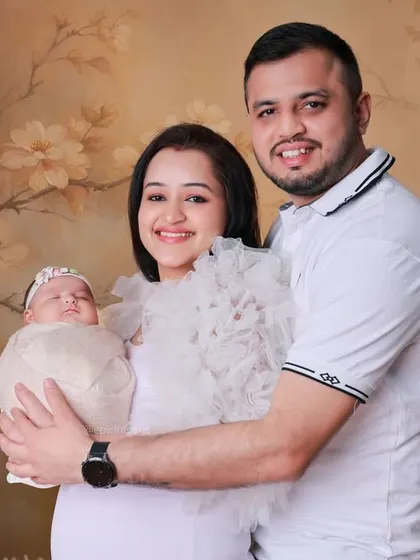 A happy family of three posing against a soft, floral backdrop. We offer various backdrops and styles to create classic family portraits that celebrate your new addition.