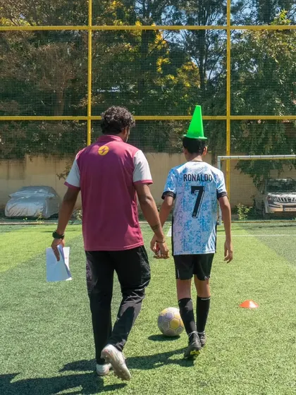 A coach walks hand-in-hand with a young player wearing a cone as a party hat. This image perfectly captures the fun, caring, and lighthearted spirit of our academy.