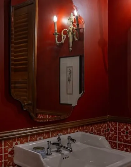 Another view of the dramatic red bathroom in Dhaka. The space is layered with art and vintage-style sconces, proving that even a functional room can be a place to express your personality.