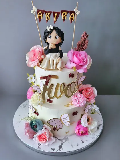 Butterflies and flowers for lil Akira's second birthday. This two-tier cake is a floral fantasy, with a custom figurine and delicate butterfly accents.