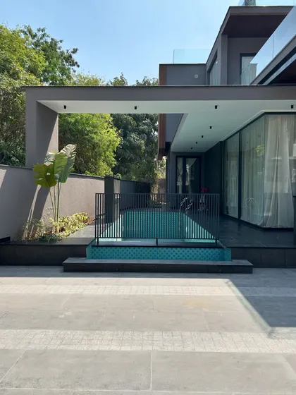 At Gulmohar Farmhouse, the swimming pool is tucked alongside the home, creating a private and accessible aquatic retreat. A simple metal railing provides safety without obstructing the view, and a large canopy offers a shaded area for poolside lounging.