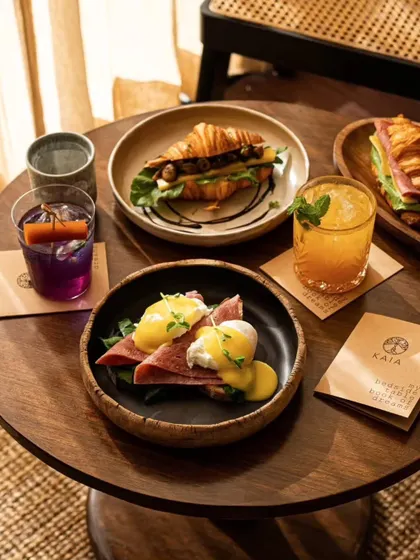 An intimate table setting at Kaia Goa, featuring Eggs Benedict and croissant sandwiches. The warm, woody tones and branded napkins create a cozy and branded experience.