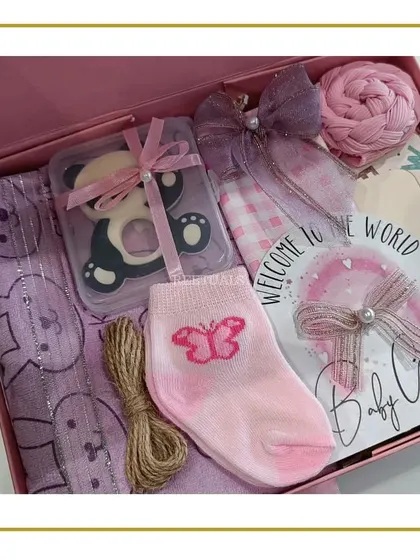 The full baby girl gift set in a pink box, including a teether, socks, a swaddle, and a 'Welcome to the World' card.
