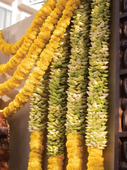 Traditional flower garlands, or 'thomalas', made of marigolds and woven leaves, are used to frame the backdrop. This element adds an authentic South Indian touch and a beautiful texture to the overall design.