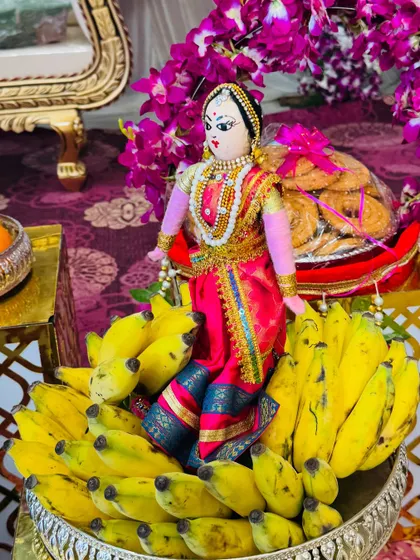 A traditional offering of bananas and sweets, beautifully arranged with a doll dressed in a pink saree. The combination of fresh fruit and decorative elements makes the platter special.