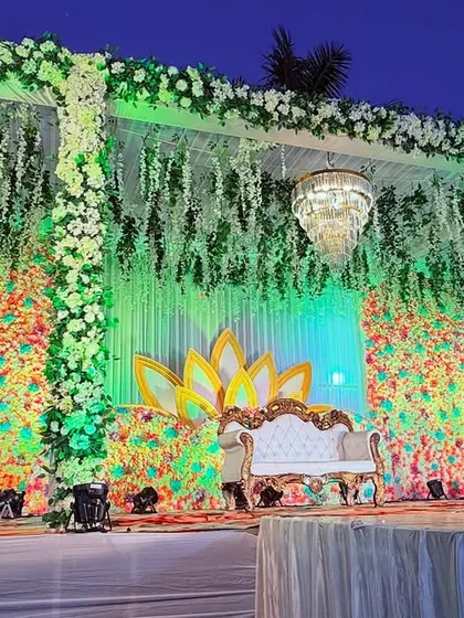 The same colorful floral stage seen from a different angle, highlighting the hanging chandeliers and the lush greenery.