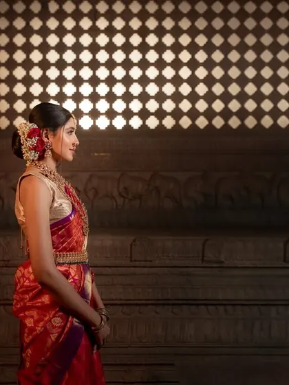 A classic bridal portrait within a temple. The side lighting beautifully highlights the bride's profile and the intricate details of her silk saree and floral hair adornments.