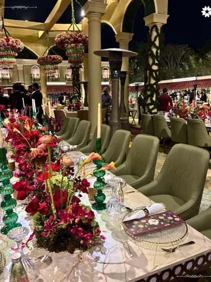 A long view of the dining tables at the Sangeet. The repetition of the floral arrangements and place settings creates a powerful visual rhythm, emphasizing the scale and elegance of the event.