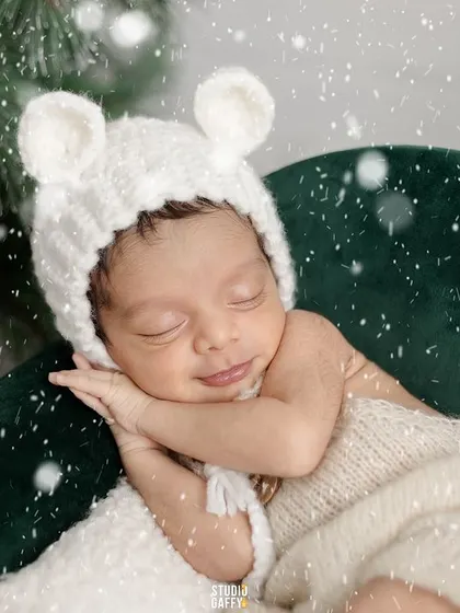 A winter wonderland dream. This newborn, wearing an adorable bear-ear hat, sleeps peacefully amidst a snowy Christmas scene.