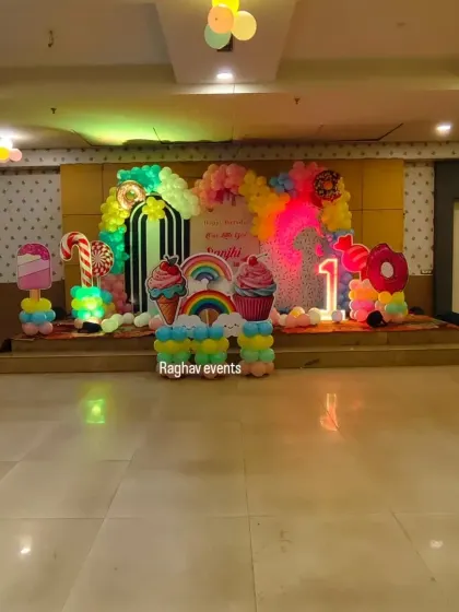 A wider view of the candyland themed birthday party stage. The decoration includes large candy and ice cream cutouts, a balloon arch, and a light-up number '1'.