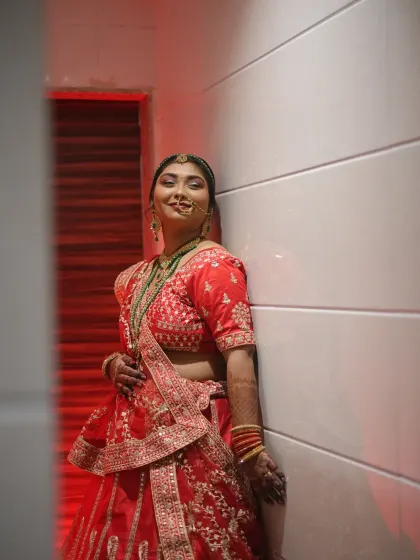 A full-length bridal portrait with dramatic red lighting. This shot captures the bride's confident pose and the stunning details of her red lehenga.