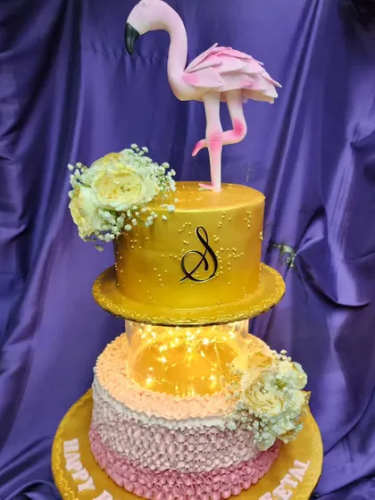 This two-tier flamingo cake features a lighted separator for a magical glow. The top tier is finished in a brilliant gold, making it a glamorous and eye-catching centerpiece for a birthday party.